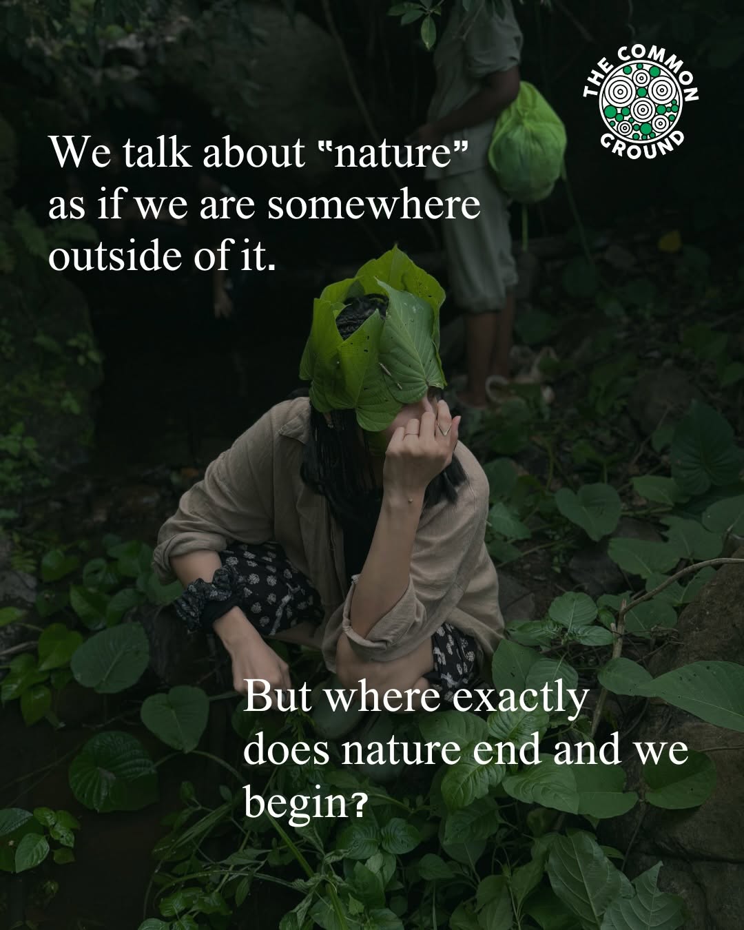 A woman crouching among large leaves that cover her face, in dense green forest. Another person stands behind with a bright green bundle.